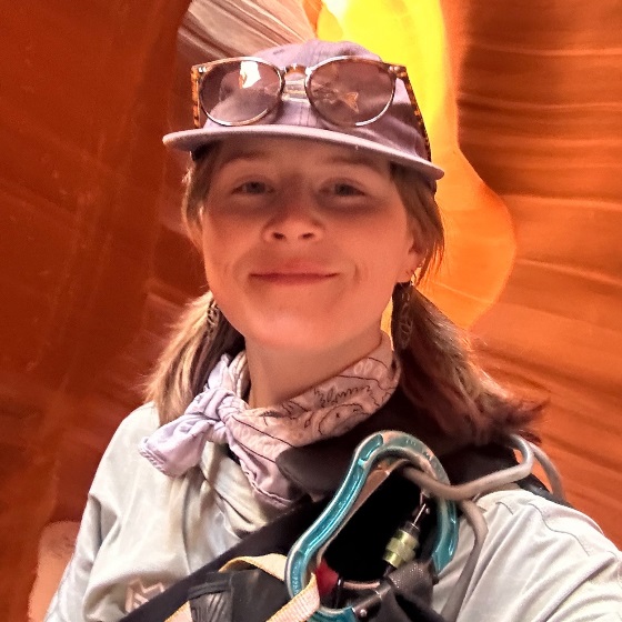 Christina Waddle, Field Ecologist, stands wearing outdoor attire in front of an orange rock formation.